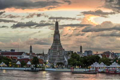 Buildings at waterfront against cloudy sky