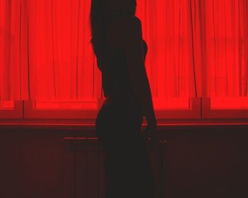 Midsection of woman standing by red window curtain at home