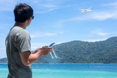 Man flying drone over river by mountain against sky