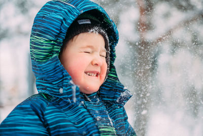 Little boy in blue striped winter clothes squinting when snow flies in his face