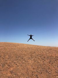 Man jumping flying over landscape against clear blue sky