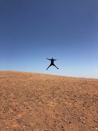 Man jumping flying over landscape against clear blue sky