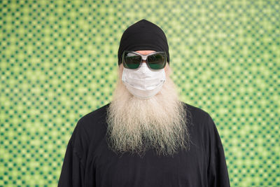 Portrait of man wearing sunglasses standing against green background