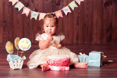 Cute baby girl with cake sitting on floor
