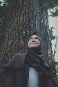 Smiling girl standing against tree trunk