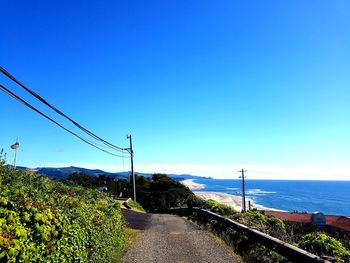 Road by sea against clear blue sky