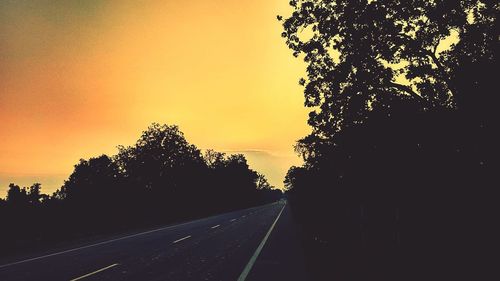 Road amidst silhouette trees against clear sky during sunset