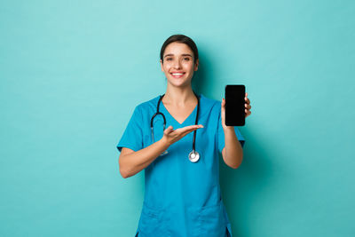 Portrait of smiling doctor holding mobile phone against colored background