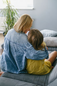 Rear view of mother and daughter sitting on sofa at home