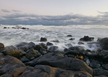 Rocks in sea against sky during sunset