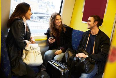 Happy young friends talking while traveling in yellow train