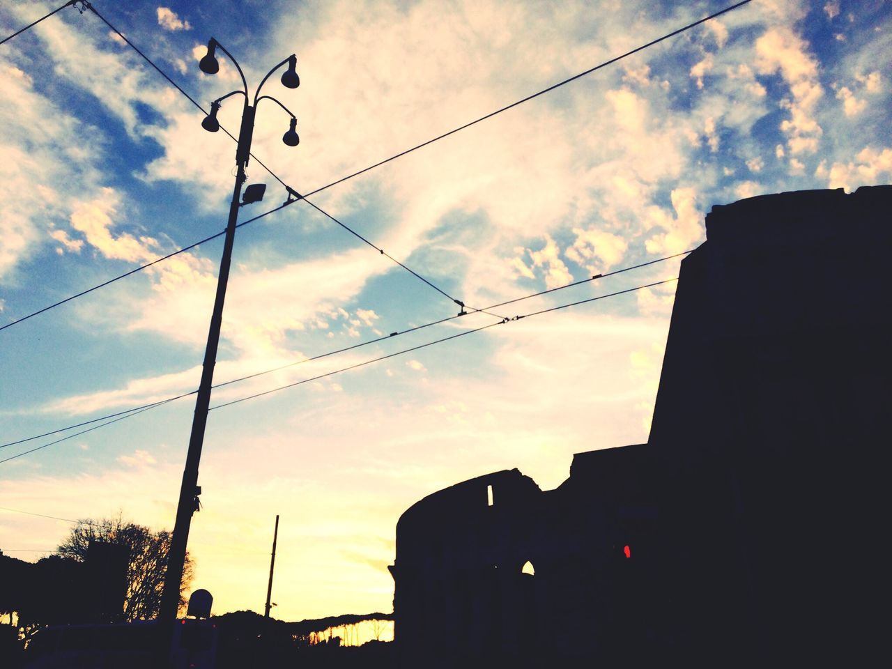 power line, low angle view, sky, building exterior, architecture, built structure, cable, silhouette, sunset, street light, electricity, cloud - sky, electricity pylon, connection, power supply, cloud, lighting equipment, cloudy, city, power cable