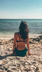 Rear view of woman sitting at beach against sky