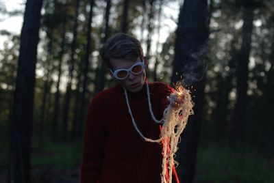 Young man holding sparkler standing in forest