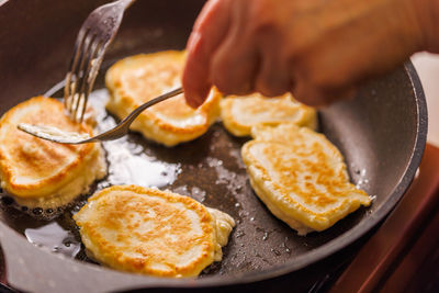 Hands with two forks flipping semi-liquid dough roasting on cast iron pan covered with vegetable oil
