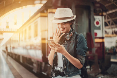 Young woman looking through mobile phone while standing on laptop