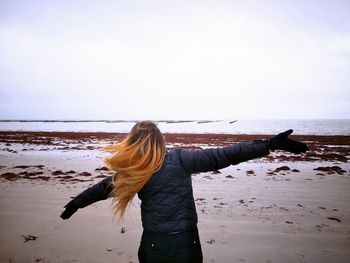 Rear view of woman standing at beach against sky