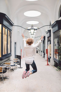 Full length rear view of woman jumping in building corridor