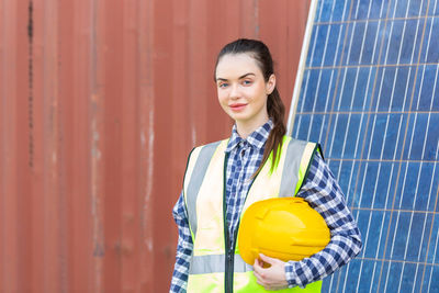 Portrait of a smiling young woman standing against wall