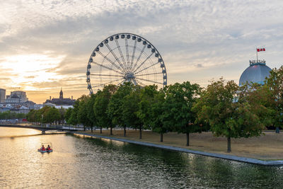 Ferris wheel by river against cloudy sky