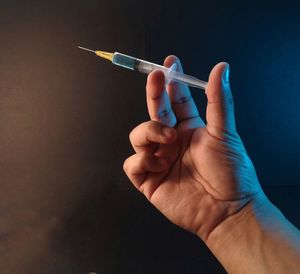 Close-up of hand holding cigarette against gray background