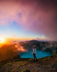 Rear view of man standing on land against sky during sunset