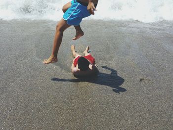 Low section of boy jumping over friend at beach