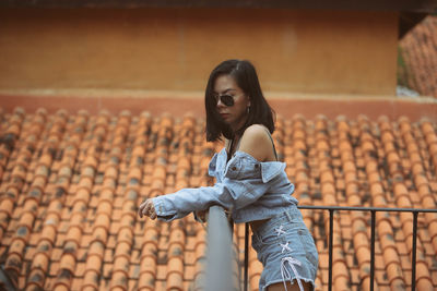 Fashionable woman in sunglasses standing against roof tiles