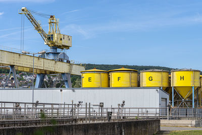 A large port crane on rails standing on the loading yard, visible yellow silos.