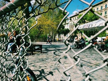 People at sidewalk cafe on footpath seen from damaged chainlink fence