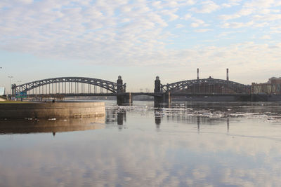 Bridge over river in city against cloudy sky