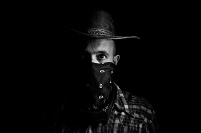 Portrait of man wearing mask and hat against black background