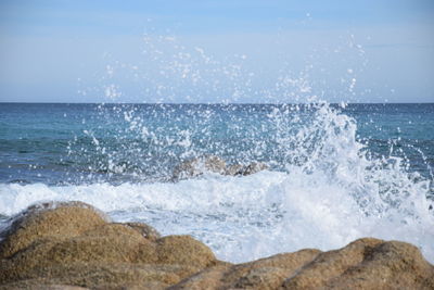 Waves splashing on rocks at shore against sky