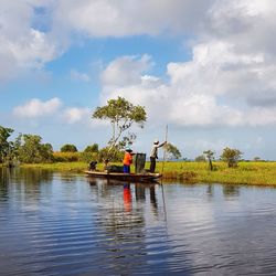 Fishermen sailing boat in lake against cloudy sky