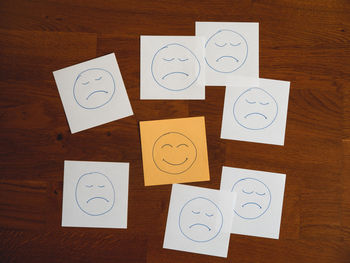 High angle view of happy face note among sad emoticons