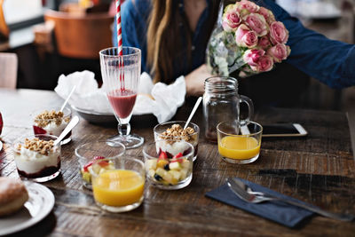 Midsection of woman sitting with flower bouquet by food on dining table at restaurant