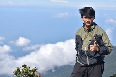 Portrait of young man gesturing thumbs up on mountain against sky