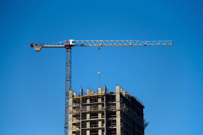 Low angle view of crane against clear blue sky