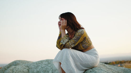 Disappointed young girl thinks about the end of summer sitting on a rock