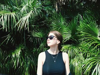 Portrait of young woman wearing sunglasses standing against plants
