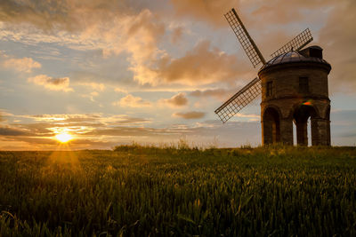 Traditional windmill on field against sky during sunset