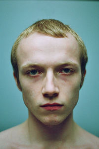 Close-up portrait of shirtless young man against turquoise background