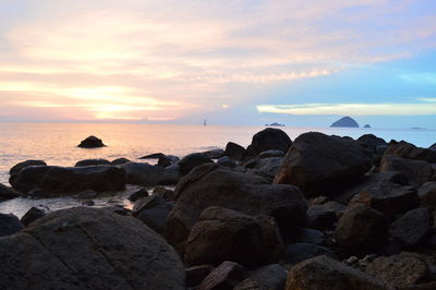 Rocks on beach against sky during sunset