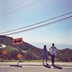 Rear view of friends standing by road sign on footpath