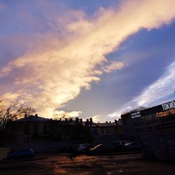 Cars on street by buildings against sky at sunset