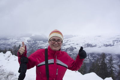 Portrait of woman gesturing thumbs up against snowcapped mountains