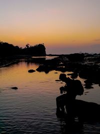 Silhouette men on lake against clear sky during sunset