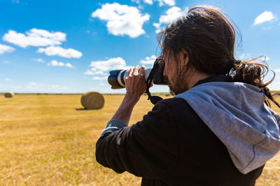 Rear view of man photographing on field against sky