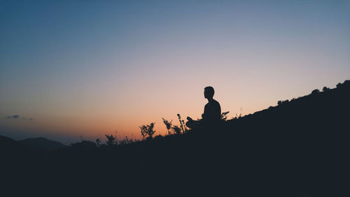 Silhouette man sitting on field against sky during sunset