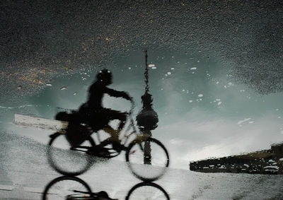 Upside down image of woman riding bicycle reflecting in puddle